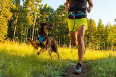 a man running with his dog on a trail in the woods during the day time