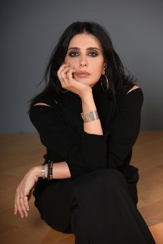 a woman sitting on the floor with her hand under her chin and looking at the camera