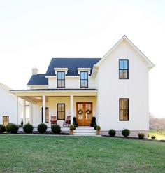 a large white house with black roof and two story windows on the front porch, surrounded by green grass