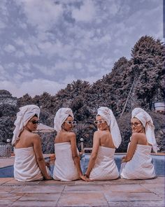 three women sitting next to each other near a swimming pool wearing towels on their heads