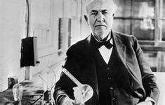 an old man in a suit and bow tie standing next to a desk with a laptop on it