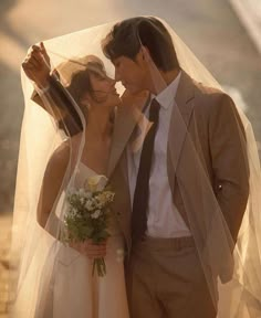 a bride and groom kissing under a veil on their wedding day in the sun light