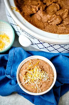 a bowl of brownie dip with cheese on top and a blue towel next to it