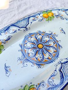 an ornate blue and white plate with oranges on it sitting on a table cloth