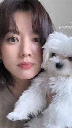 a woman holding a small white dog in her arms and looking at the camera with an intense look on her face