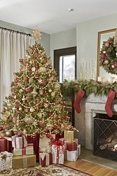 a decorated christmas tree in front of a fire place with presents under it and stockings on the mantel