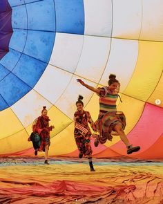 three people in colorful clothing are running through a hot air balloon