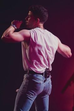 a man standing on top of a stage with his hands behind his head and holding a microphone to his ear