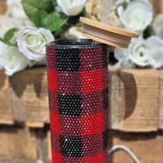 a red, black and white plaid tumbler with a wooden lid next to flowers