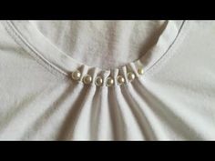 a white shirt with three pearls on the front and two beads in the back,