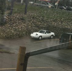 two cars are parked in a parking lot on a rainy day, one is white and the other is black