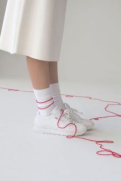 a woman's feet in white tennis shoes with red string