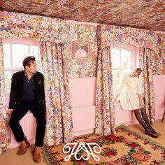 a man and woman sitting in front of a pink wallpapered room with floral curtains