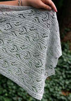 a woman holding onto a white shawl in front of some bushes and trees with her hand on it