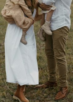 a man and woman are standing in the grass with a baby on their shoulders,