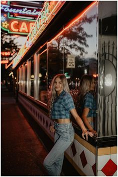 two women are standing in front of a food truck at night, posing for the camera