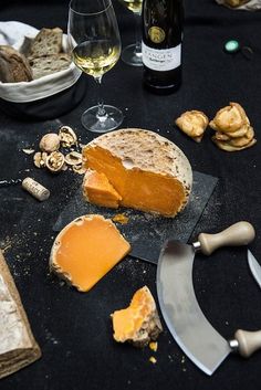 a table topped with cheese and crackers next to wine glasses, corks and bread