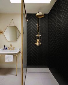 a black and white bathroom with gold fixtures on the shower head, sink and mirror