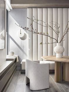 a white vase sitting on top of a wooden table next to a window covered in blinds