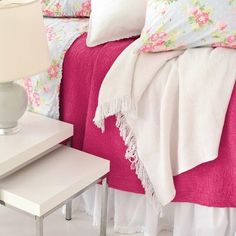 a bedroom with pink and white bedding, two nightstands and a lamp on the side table