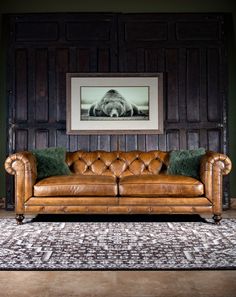 a brown leather couch sitting in front of a wooden wall with a painting on it