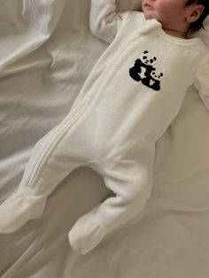 a small child laying on top of a white bed covered in sheets and pillows with a panda bear embroidered on it's chest