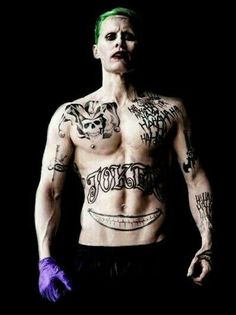 a shirtless man with tattoos on his chest and purple gloves in front of a black background