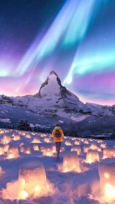 a person standing in the snow looking at an aurora bore over mountains and sky with lights