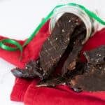 two pieces of chocolate sitting on top of a red cloth next to a green ribbon