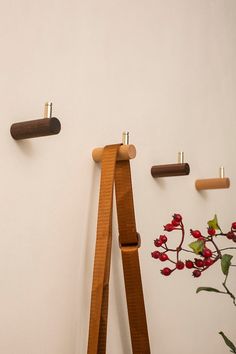 three wooden pegs are hanging on the wall next to a vase with red flowers