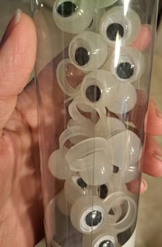 a person holding a glass container filled with lots of plastic eyeballs in it's hand