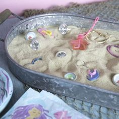 a metal tray filled with lots of sand and various toy items on top of it