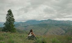 a woman sitting on top of a lush green hillside