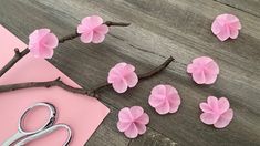 some pink flowers and scissors on a wooden table next to a piece of paper that has been cut out