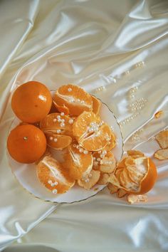 oranges and other fruit on a plate with white satin material behind them, all scattered together