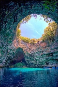 the entrance to an underground cave with blue water and trees on either side, looking up into the sky