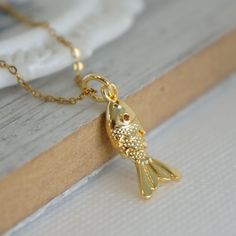 Gold Fish Charm Necklace, Koi Pendant, Dainty Fish Jewelry, Cute Gift For Her, Animal Lover Gift, Ocean Lover Gift Necklace for Women Dive into a sea of whimsical style with our Gold Fish Charm Necklace, a delightful piece that captures the essence of the ocean. This charming accessory features a dainty gold fish adorned with a vibrant orange zircon eye that sparkles with every movement.  Perfect for the ocean lover in you, this necklace exudes a playful elegance that adds a touch of fun to any outfit. Whether you're heading to the beach or simply want to channel marine-inspired fashion, this cute charm necklace is a versatile piece that will effortlessly elevate your look.  Embrace the enchanting allure of the underwater world with this eye-catching accessory that will surely make a splas Gold Ocean-inspired Charm Necklaces As Gift, Fish Charm Necklace, Gold Fish-shaped Necklace For Gift, Fish Pendant Gold, Fish-shaped Charms Necklace Gift, Enamel Fish-shaped Jewelry For Gifts, Cute Gifts For Her, Fish Jewelry, Fish Necklace