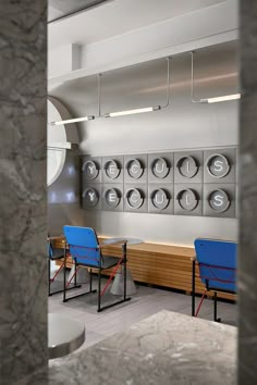 two blue chairs sitting in front of a wall with clocks on it's sides