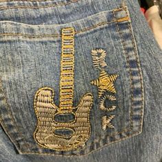 the back pocket of someone's jeans with an embroidered guitar on it and gold trimmings