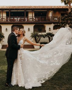 a bride and groom kissing in front of a large building with palm trees on the lawn