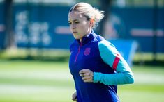 a woman is running on the grass with her arm around her neck and wearing a blue shirt