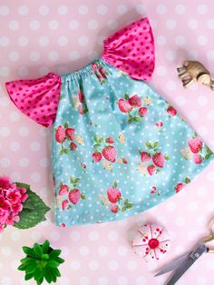 a pink and blue dress with strawberrys on it next to scissors, flowers and other items