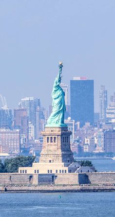 the statue of liberty in new york city is seen from across the water with skyscrapers in the background