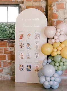 an arch with balloons and pictures on it in front of a brick wall that says a year with someone born