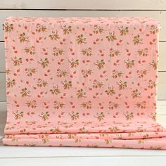 a pink blanket with cherries on it and white wood boards in the back ground