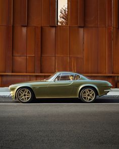 a green sports car parked in front of a tall building with brown panels on it's side