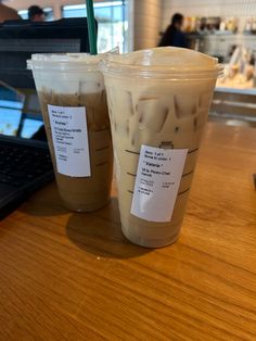 two iced drinks sitting on top of a wooden table next to a laptop computer in a restaurant