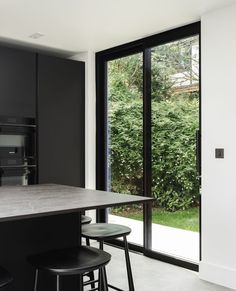 a kitchen with black cabinets and stools next to an open door that leads outside