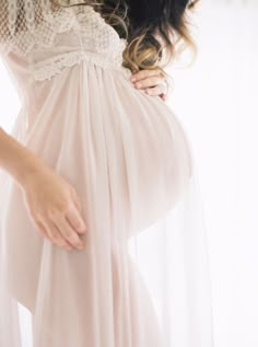 a pregnant woman wearing a white dress and holding her belly