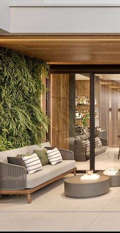 a living room filled with lots of furniture next to a wall covered in greenery